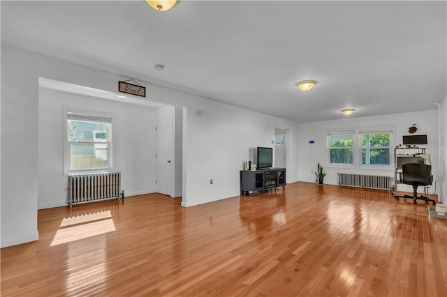 unfurnished living room with a wealth of natural light, radiator, and wood-type flooring