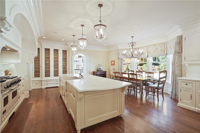 kitchen featuring hanging light fixtures, dark hardwood / wood-style flooring, crown molding, range with two ovens, and a center island with sink