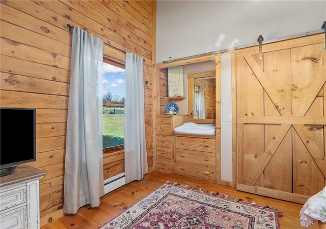 interior space with a barn door, light hardwood / wood-style floors, a baseboard radiator, and wooden walls