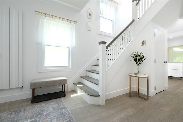 staircase featuring hardwood / wood-style flooring, a healthy amount of sunlight, and radiator heating unit