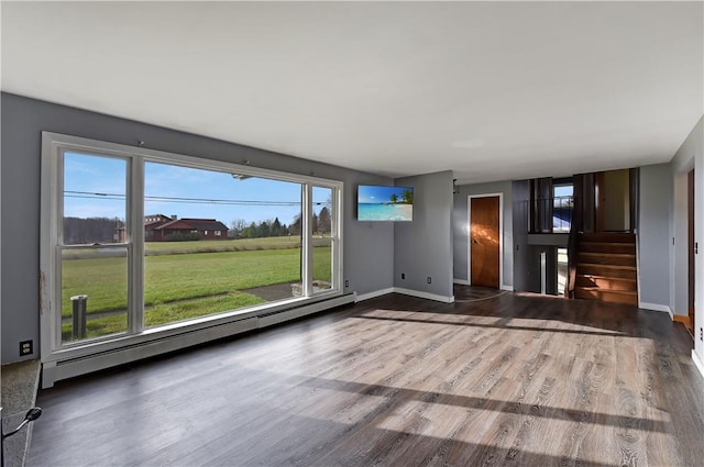 unfurnished living room featuring a wealth of natural light, baseboard heating, and wood-type flooring