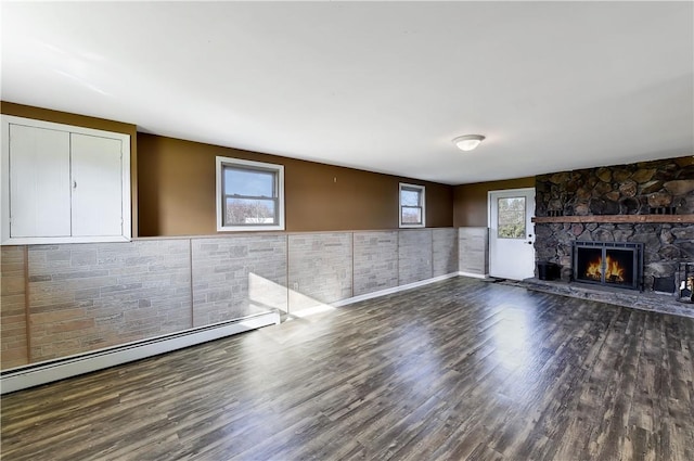 unfurnished living room with a fireplace, baseboard heating, tile walls, and dark wood-type flooring