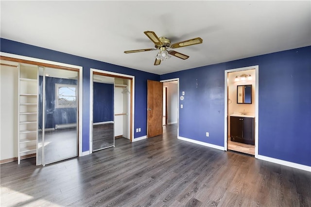 unfurnished bedroom featuring ensuite bathroom, sink, dark hardwood / wood-style floors, ceiling fan, and multiple closets