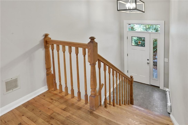 entrance foyer featuring light hardwood / wood-style flooring, a baseboard radiator, and a notable chandelier