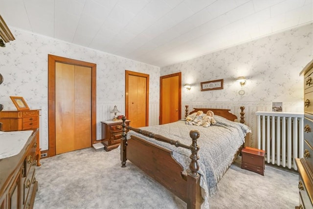 bedroom with two closets, light colored carpet, and radiator