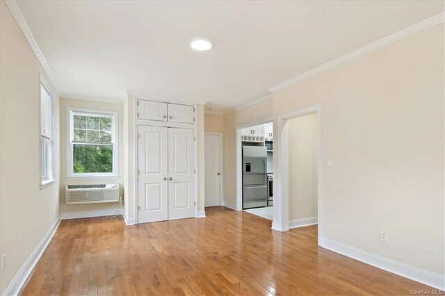 unfurnished bedroom featuring a wall unit AC, crown molding, high quality fridge, and light hardwood / wood-style flooring