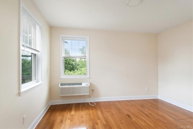 unfurnished room with a wall mounted air conditioner, plenty of natural light, and light wood-type flooring