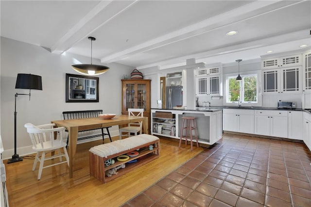 kitchen with pendant lighting, a kitchen bar, white cabinetry, stainless steel refrigerator, and beamed ceiling