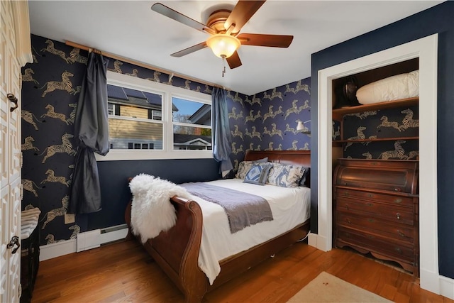 bedroom with hardwood / wood-style floors, a baseboard heating unit, and ceiling fan