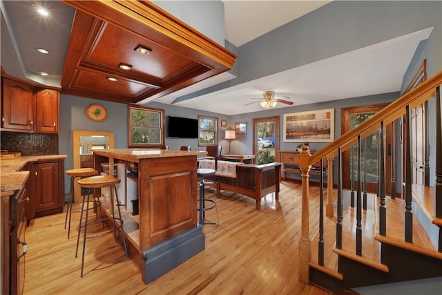 interior space with light wood-type flooring, light stone countertops, ceiling fan, a kitchen bar, and decorative backsplash