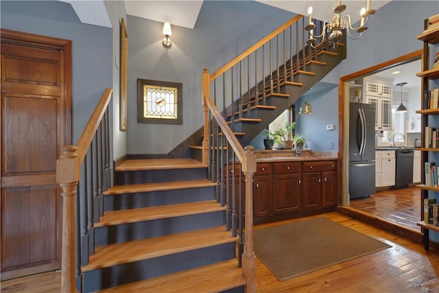 stairway with sink, an inviting chandelier, and hardwood / wood-style flooring