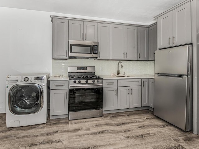 kitchen with sink, light hardwood / wood-style floors, washer / dryer, gray cabinets, and appliances with stainless steel finishes