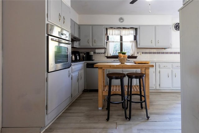 kitchen featuring tasteful backsplash, white cabinets, light wood-type flooring, and appliances with stainless steel finishes