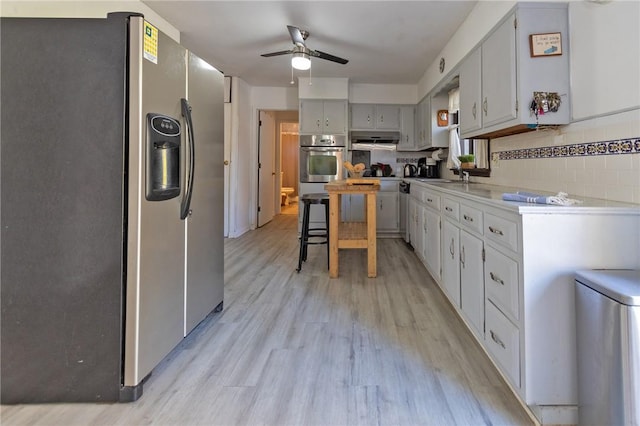 kitchen featuring ceiling fan, sink, backsplash, light hardwood / wood-style floors, and appliances with stainless steel finishes