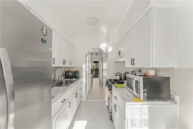 kitchen with backsplash, white cabinetry, sink, and stainless steel appliances