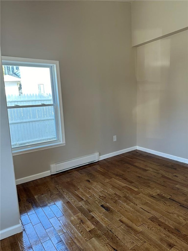 spare room featuring baseboard heating and dark hardwood / wood-style flooring