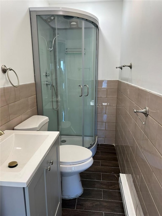 bathroom with vanity, hardwood / wood-style flooring, toilet, tile walls, and a shower with shower door