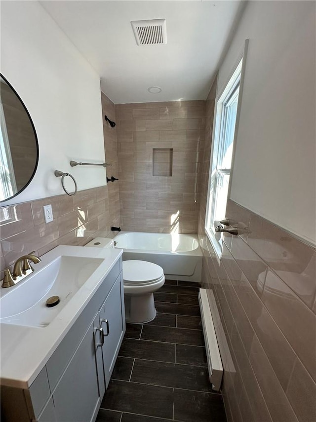 full bathroom featuring a baseboard radiator, tiled shower / bath combo, toilet, vanity, and tile walls