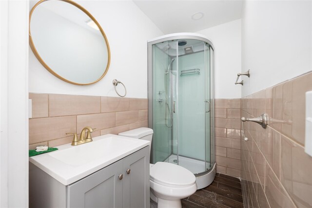 bathroom with wood-type flooring, tile walls, vanity, toilet, and a shower with door