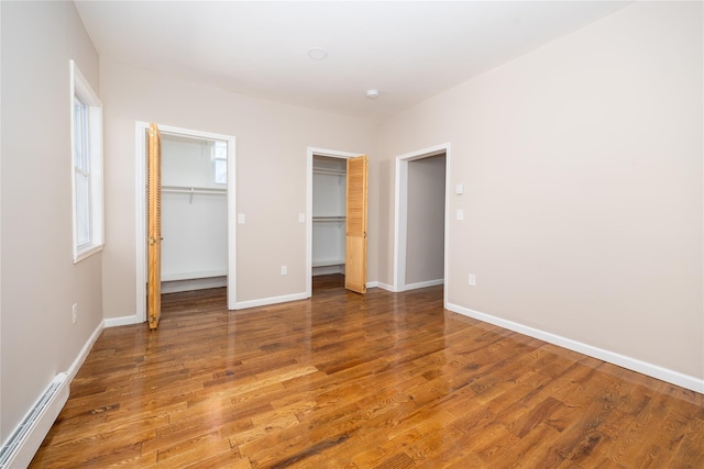 unfurnished bedroom featuring hardwood / wood-style floors, a walk in closet, and baseboard heating