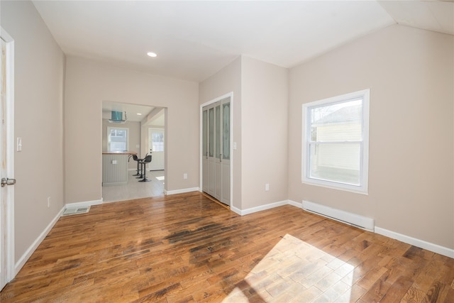 empty room featuring baseboard heating, lofted ceiling, and hardwood / wood-style flooring