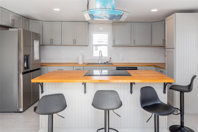 kitchen with sink, butcher block countertops, black appliances, a kitchen breakfast bar, and backsplash