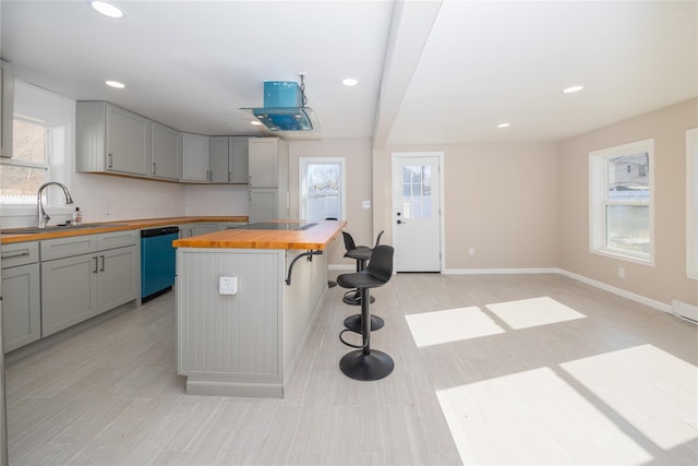 kitchen featuring a kitchen bar, butcher block counters, sink, dishwashing machine, and a wealth of natural light