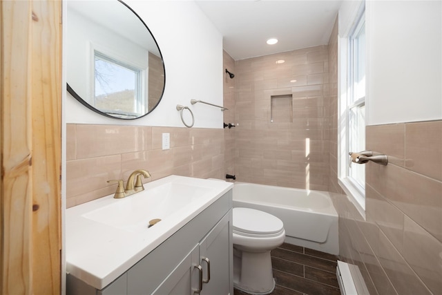 full bathroom with tile walls, tiled shower / bath combo, vanity, baseboard heating, and toilet