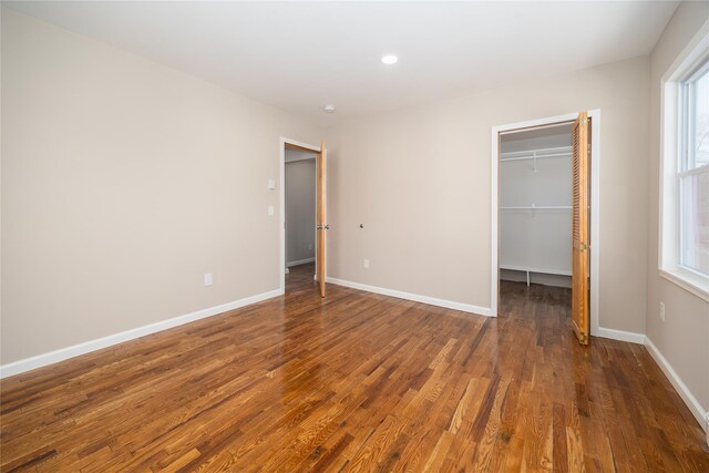 unfurnished bedroom with multiple windows, a walk in closet, and dark hardwood / wood-style floors