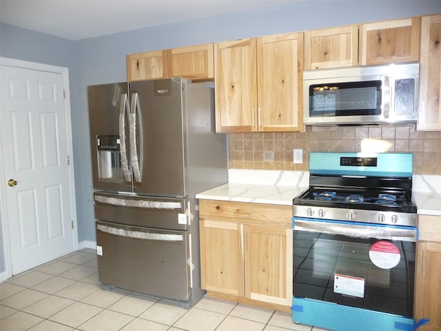 kitchen featuring light brown cabinets, light tile patterned floors, backsplash, and appliances with stainless steel finishes