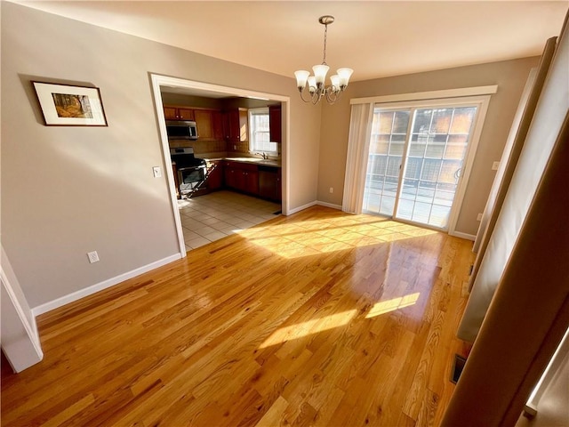 unfurnished dining area with sink, light hardwood / wood-style floors, and a notable chandelier