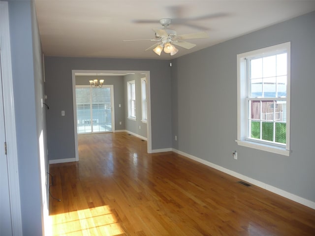 unfurnished room featuring plenty of natural light, hardwood / wood-style floors, and ceiling fan with notable chandelier