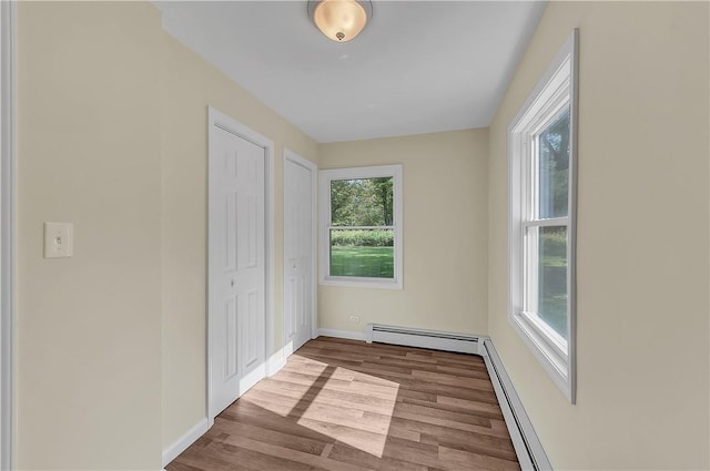 unfurnished bedroom with two closets, baseboard heating, and light hardwood / wood-style flooring