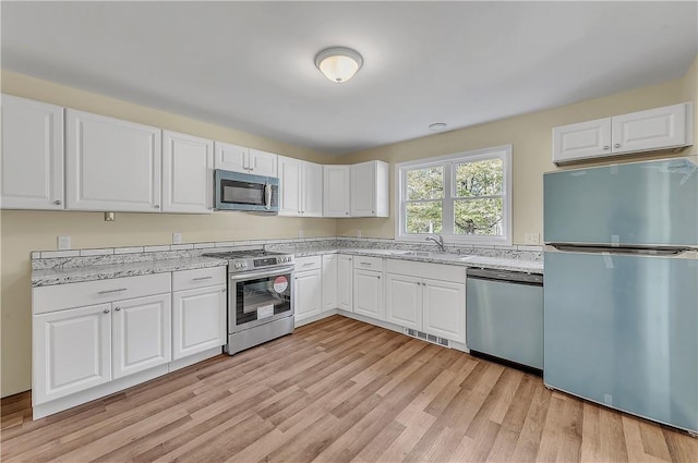 kitchen featuring light stone counters, stainless steel appliances, sink, light hardwood / wood-style flooring, and white cabinets