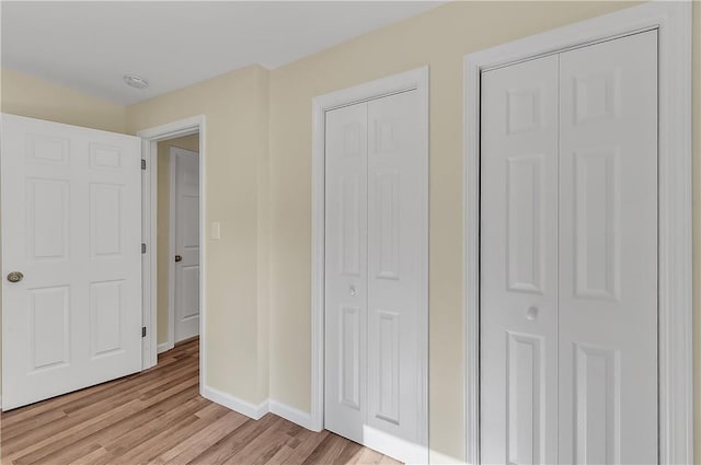 unfurnished bedroom with light hardwood / wood-style flooring and multiple closets