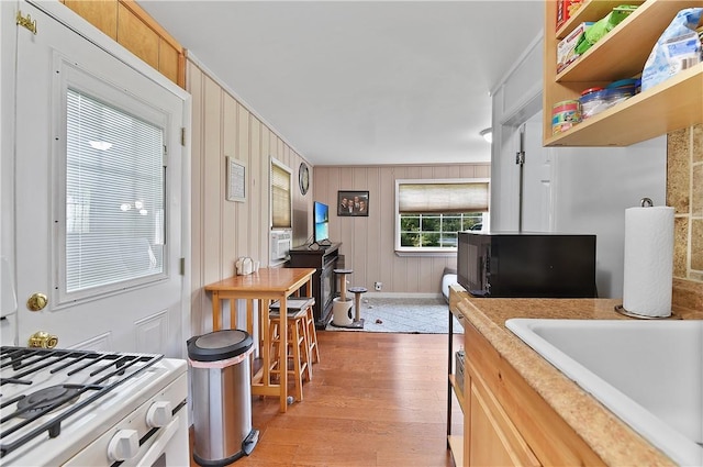 kitchen featuring sink, light brown cabinets, wooden walls, white stove, and light wood-type flooring