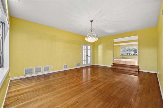 spare room with french doors, light hardwood / wood-style floors, and an inviting chandelier