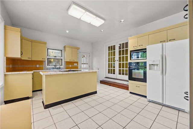 kitchen featuring built in microwave, white refrigerator with ice dispenser, a center island, oven, and tile counters