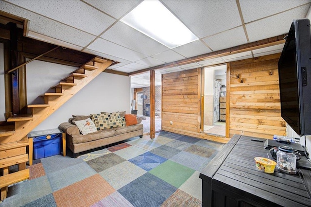 living room featuring carpet flooring, a drop ceiling, and wooden walls