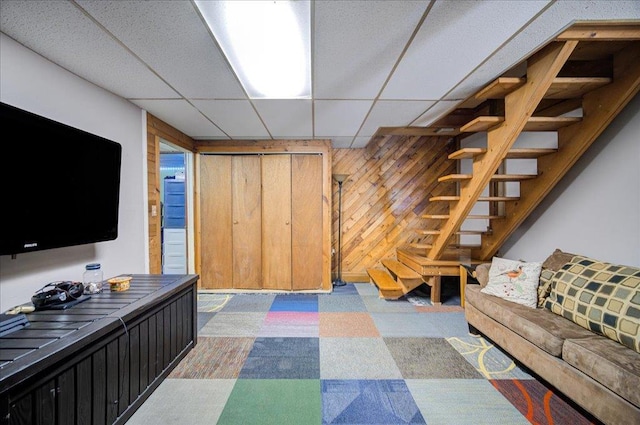 living room featuring a paneled ceiling and wooden walls