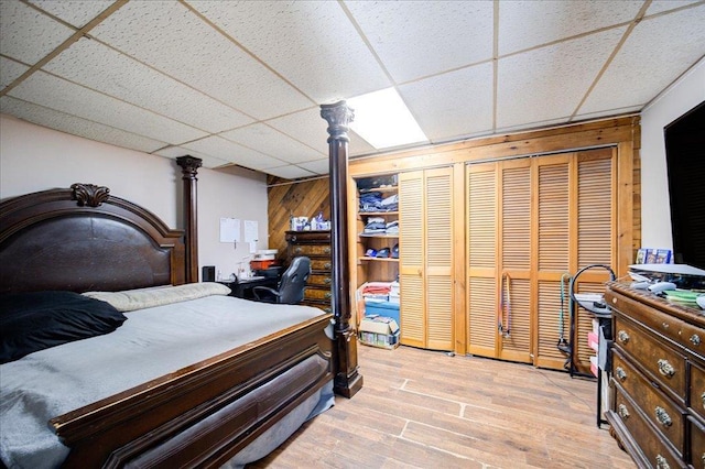 bedroom featuring wood walls, a drop ceiling, and light wood-type flooring