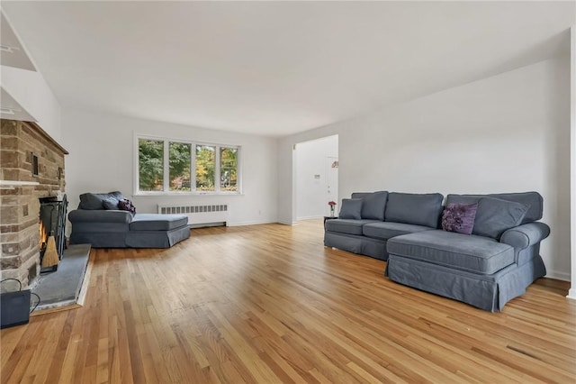 living room featuring light wood-type flooring, a stone fireplace, and radiator