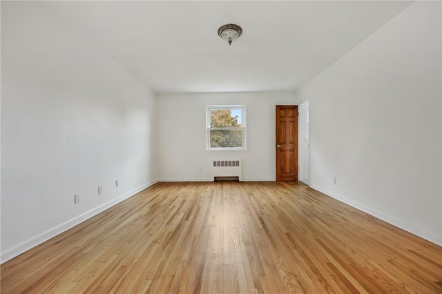 unfurnished room with radiator and light wood-type flooring