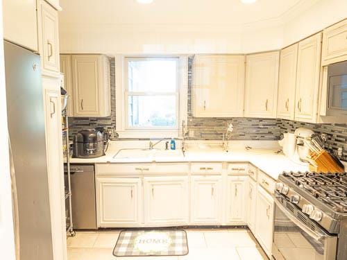 kitchen featuring backsplash, sink, light tile patterned flooring, and stainless steel appliances