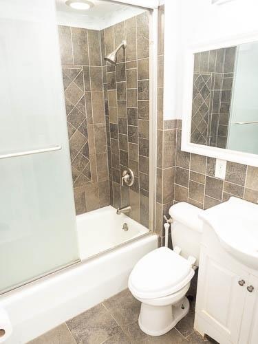 full bathroom featuring vanity, shower / bath combination with glass door, tile patterned floors, toilet, and tile walls