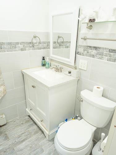 bathroom with hardwood / wood-style floors, vanity, tile walls, and toilet