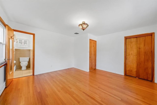 unfurnished bedroom with light hardwood / wood-style floors, connected bathroom, and a closet