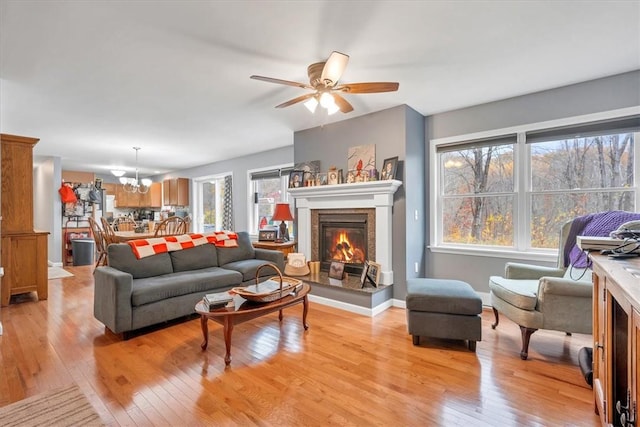 living room featuring a fireplace, ceiling fan with notable chandelier, and light wood-type flooring