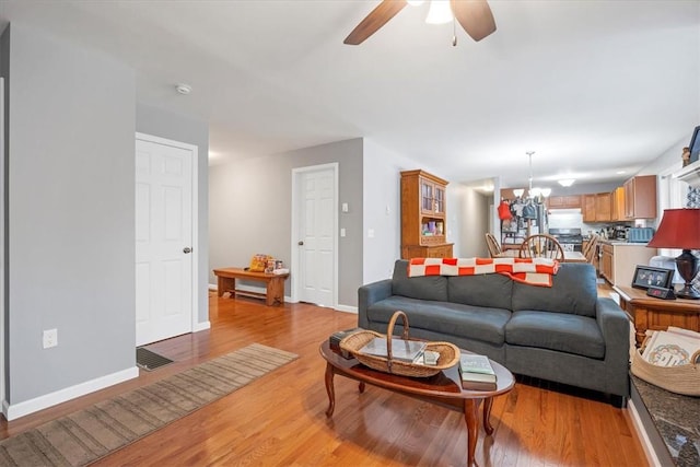 living room featuring ceiling fan with notable chandelier and light wood-type flooring