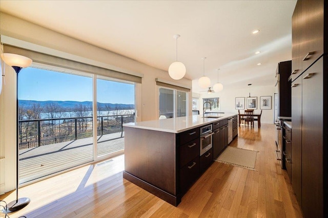 kitchen with a center island with sink, a mountain view, light wood-type flooring, and hanging light fixtures